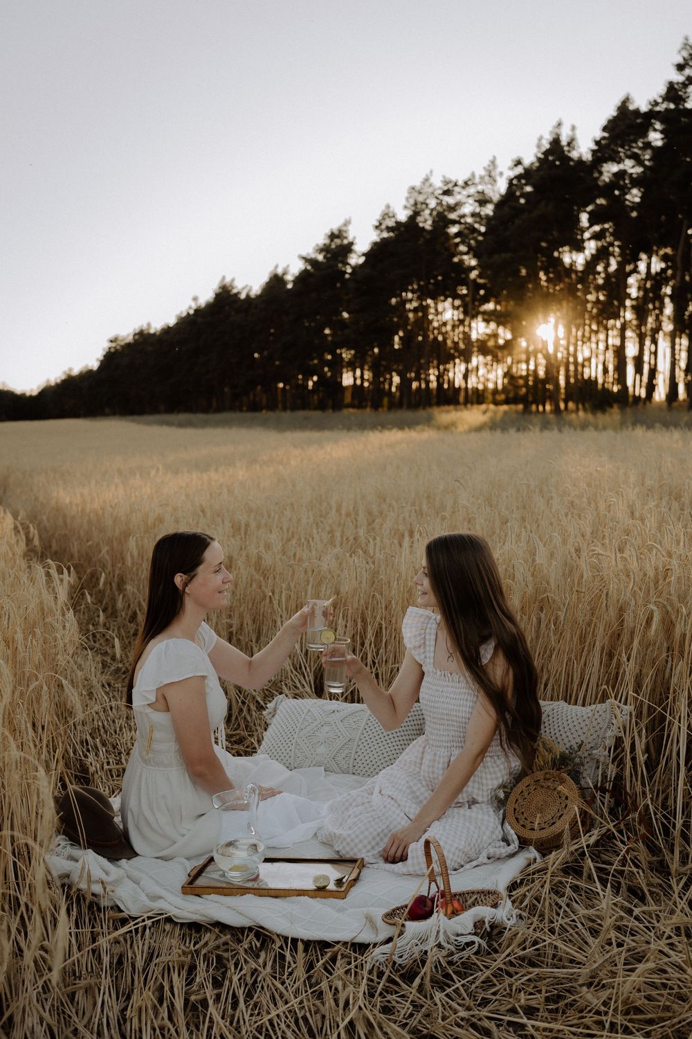 Group of people in white dresses having a sunset picnic in a golden wheat field.