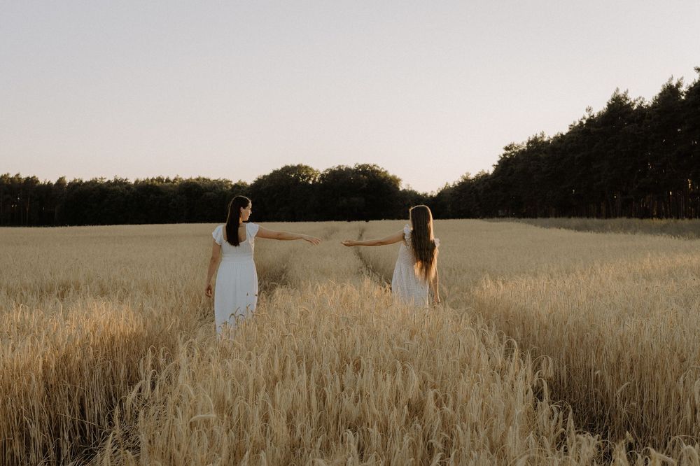 A peaceful outdoor photoshoot featuring two people standing in a golden wheat field at sunset.