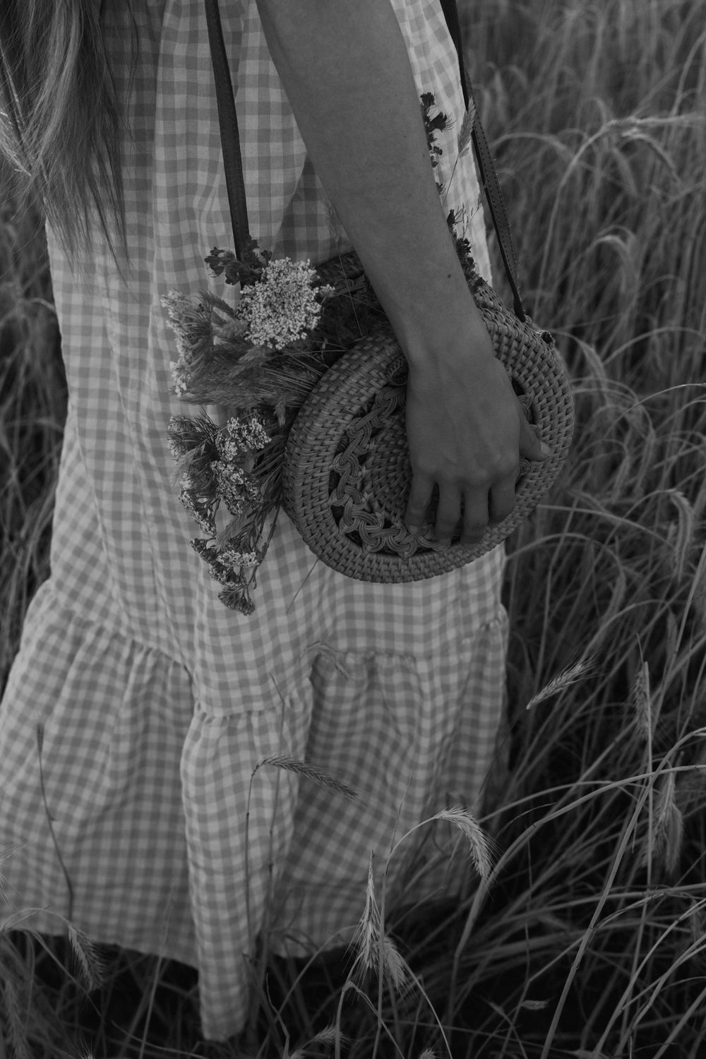A black and white photo series showing a hand holding a small woven basket against a gingham dress and tall grass.