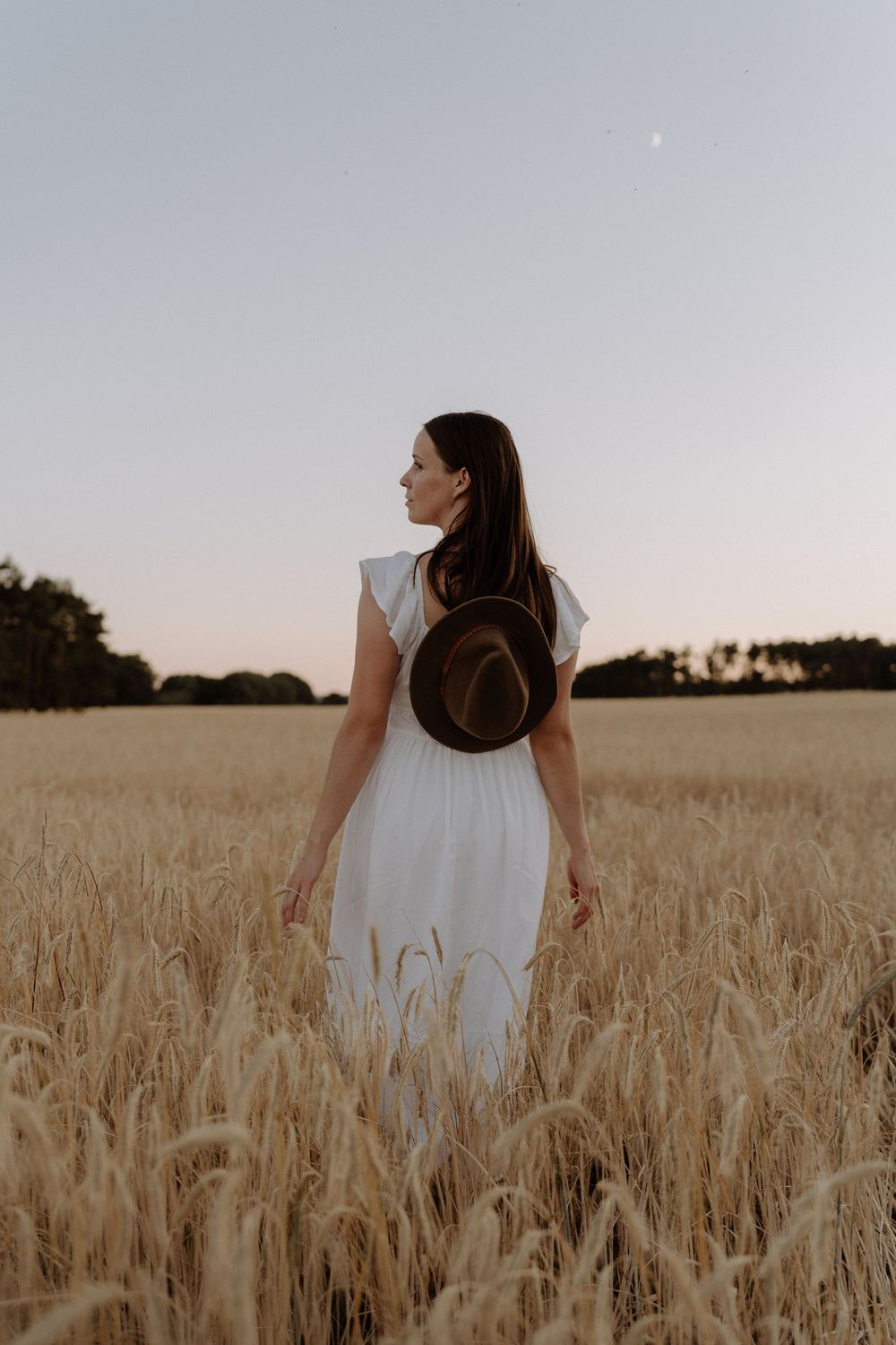Artistic candid shots of person in white dress walking through golden wheat field at sunset.
