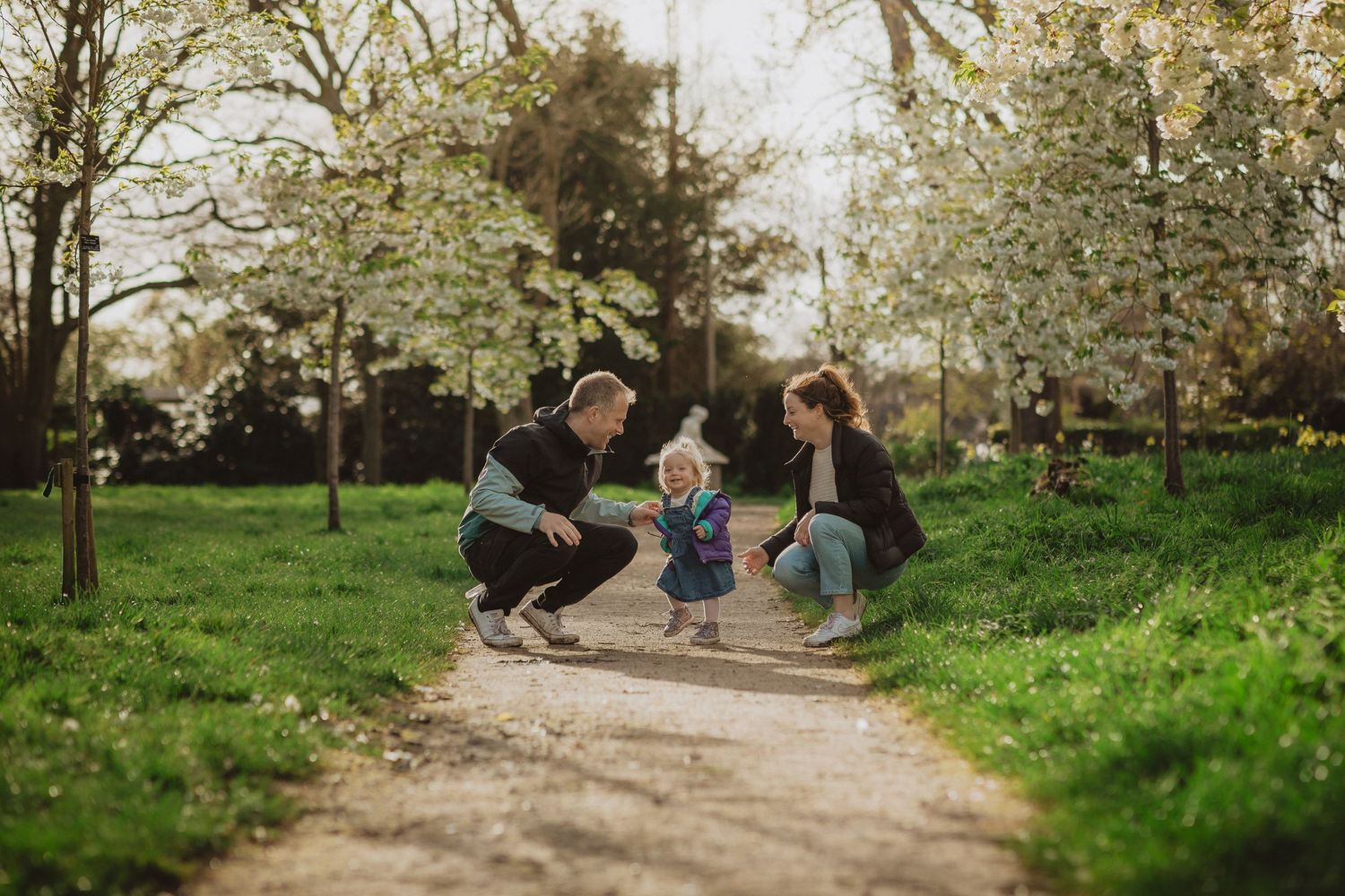 People relax on a bench under blooming cherry blossoms in a peaceful spring garden setting.