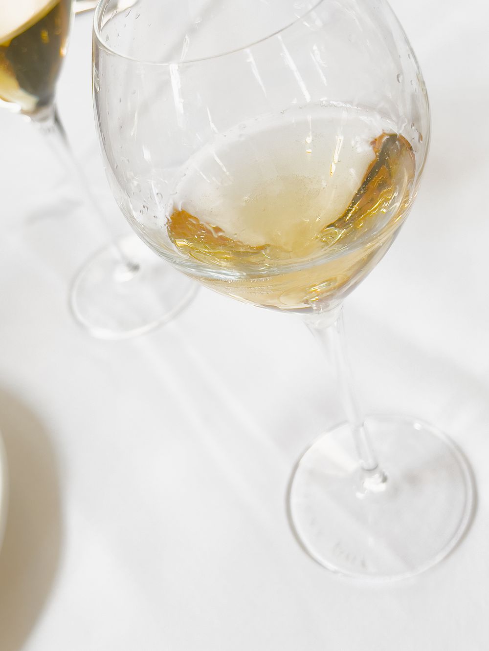 Close up view of a partially filled wine glass with white wine shown against a bright white background.