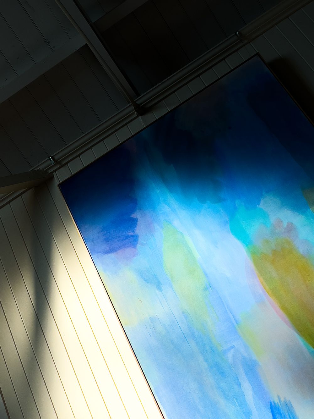 Abstract light installation with blue and yellow gradient colors against white wall creating an ethereal atmospheric effect.
