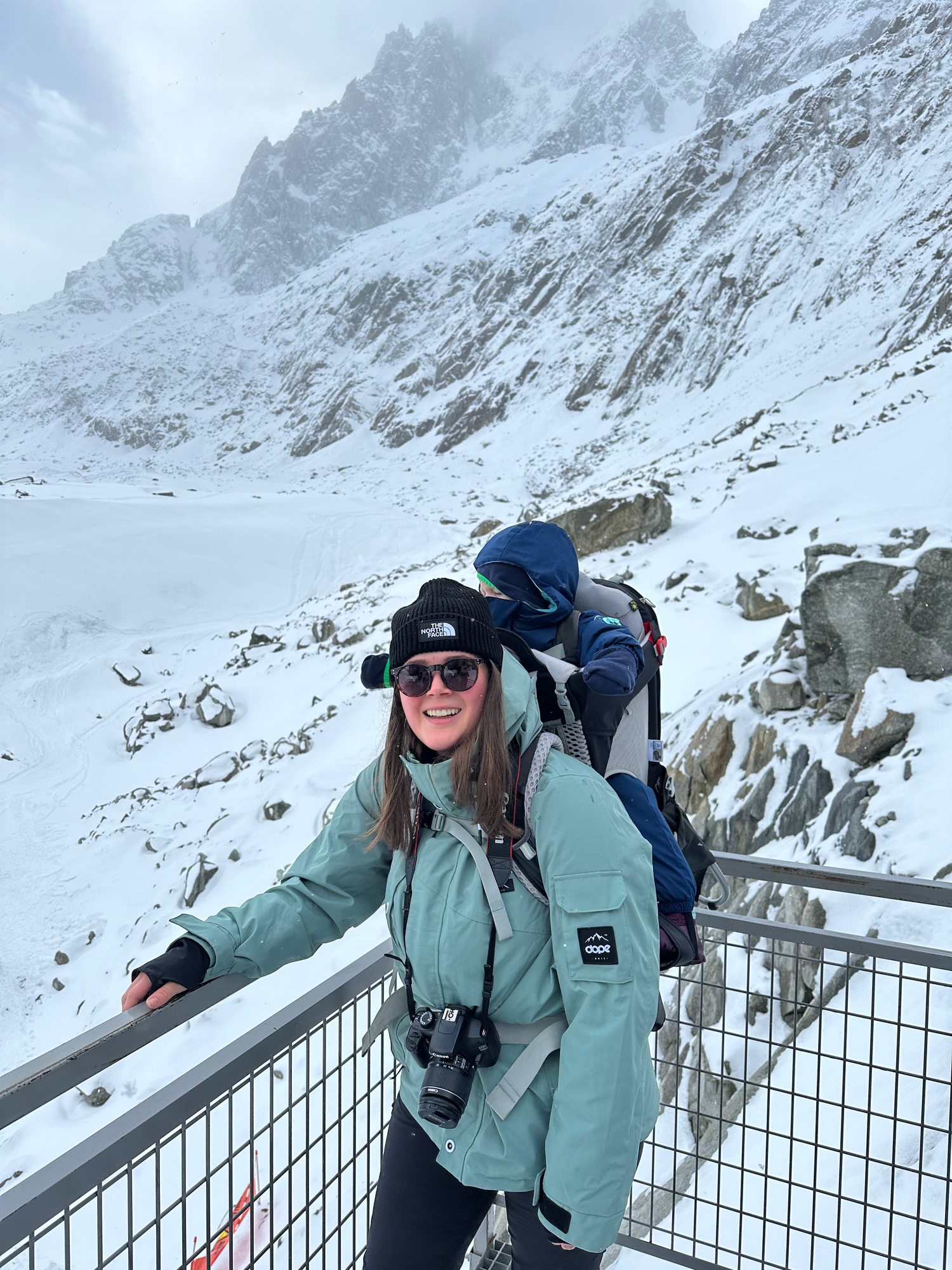 Winter adventurer poses on observation deck overlooking snowy mountain peaks.