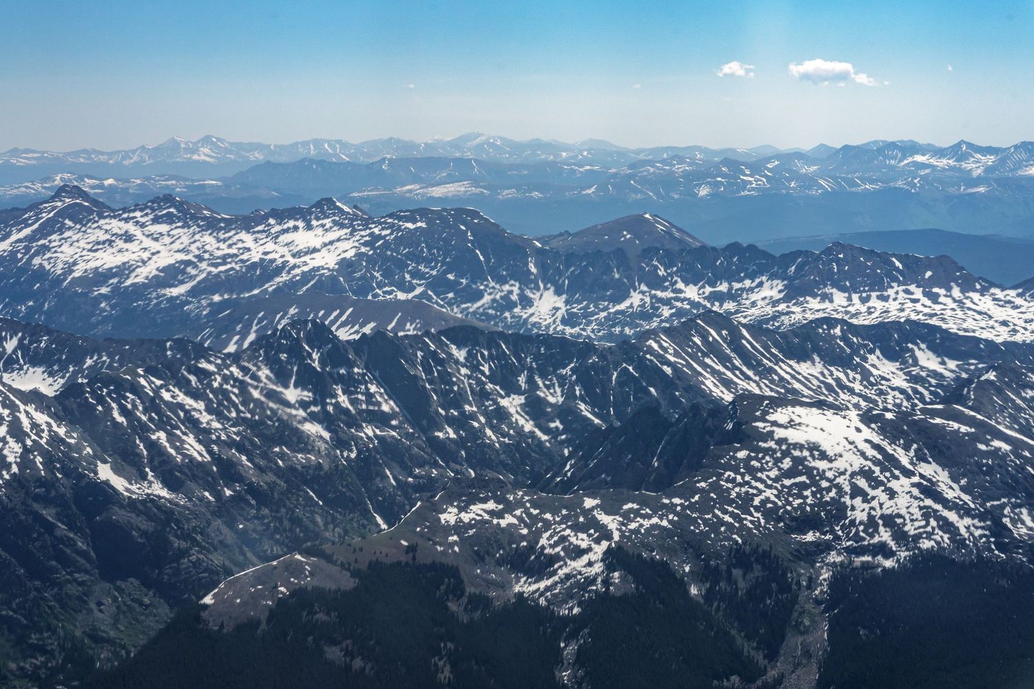Aerial view of snow-capped mountain ranges under a clear blue sky on a sunny day.