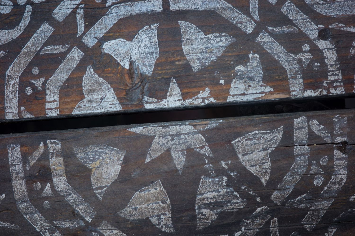Close-up of weathered dark wood panels with faded white decorative painted geometric patterns.
