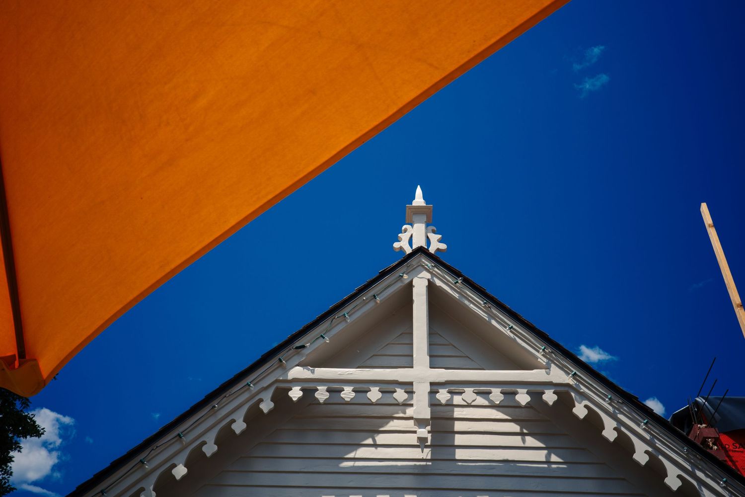 Orange umbrella canopy above a white Victorian gabled rooftop against blue sky.