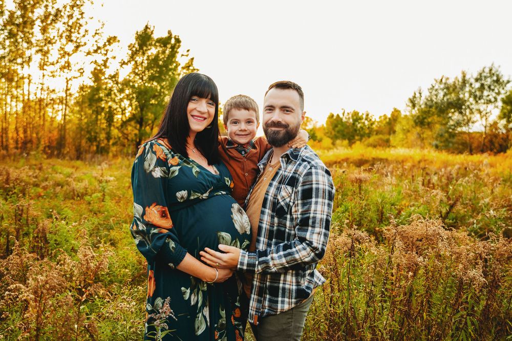 Autumn outdoor maternity photoshoot in a golden field with tall grass and trees.