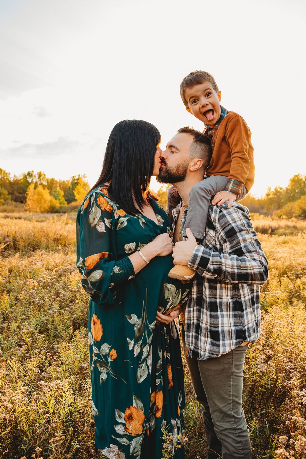 Joyful family moment captured during outdoor maternity photoshoot in autumn field.