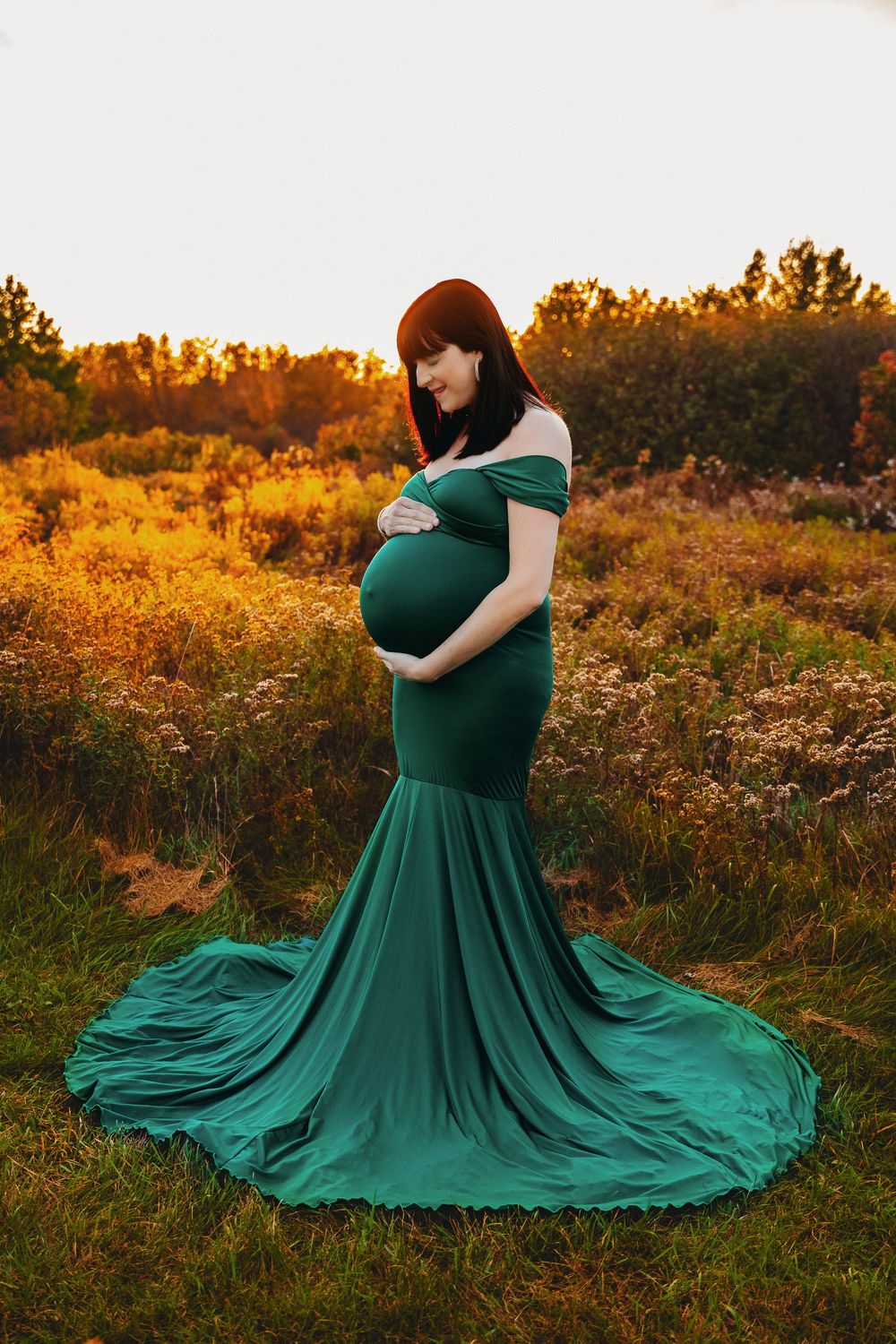Maternity portrait of woman in flowing green dress against autumn landscape.
