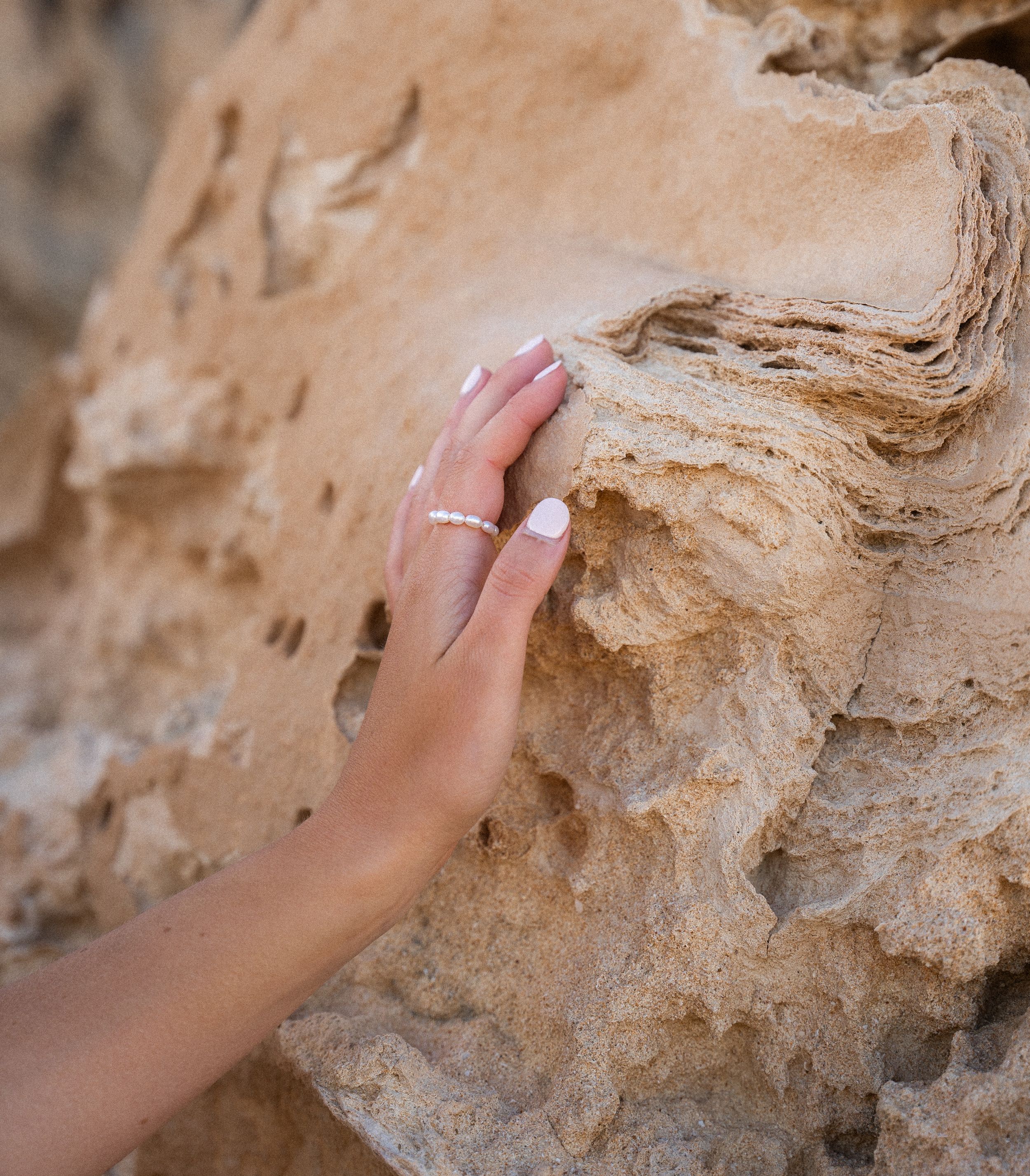 Hand with delicate rings touching textured beige rock formation.