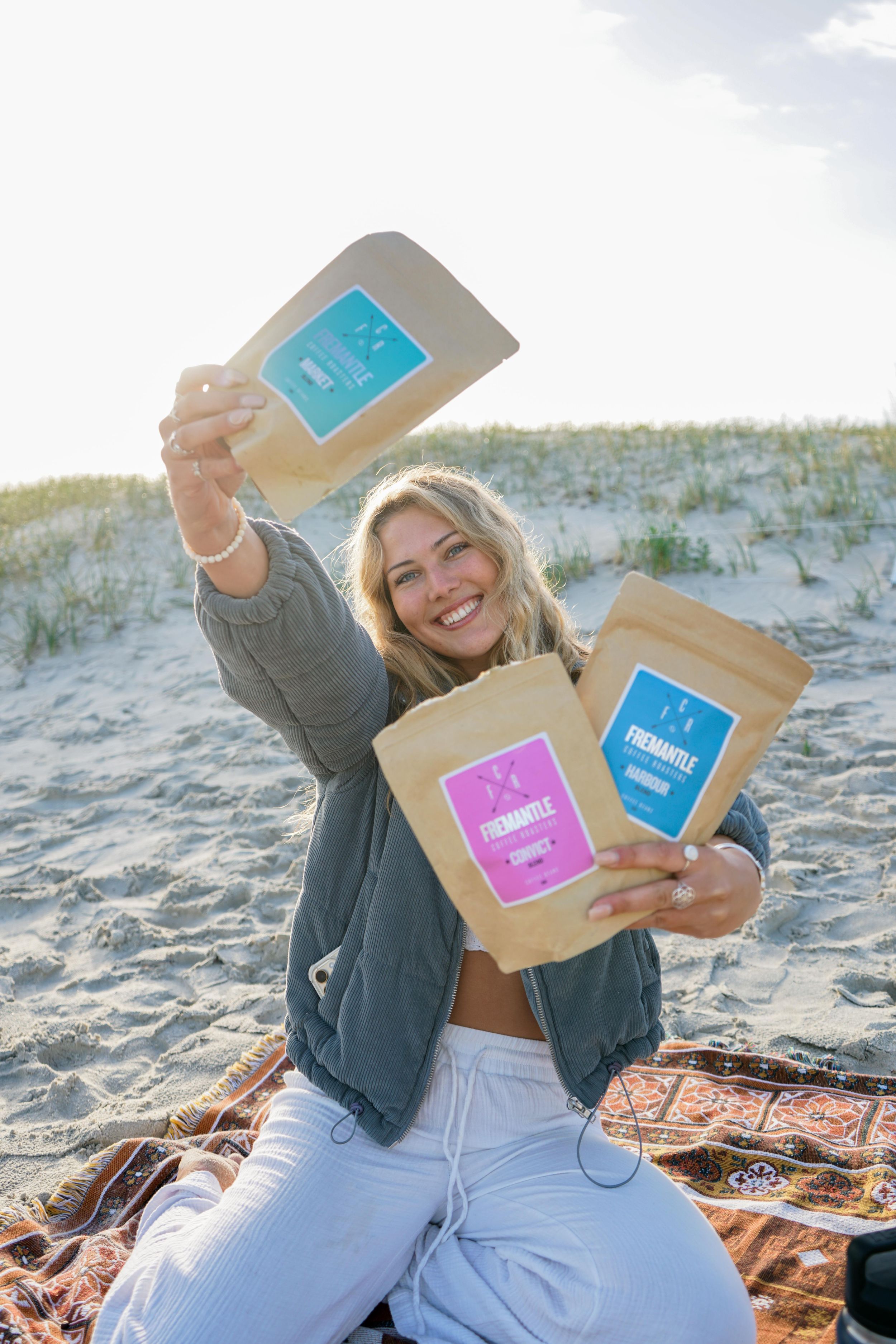 Lifestyle product photography featuring coffee packages on sandy beach blanket.
