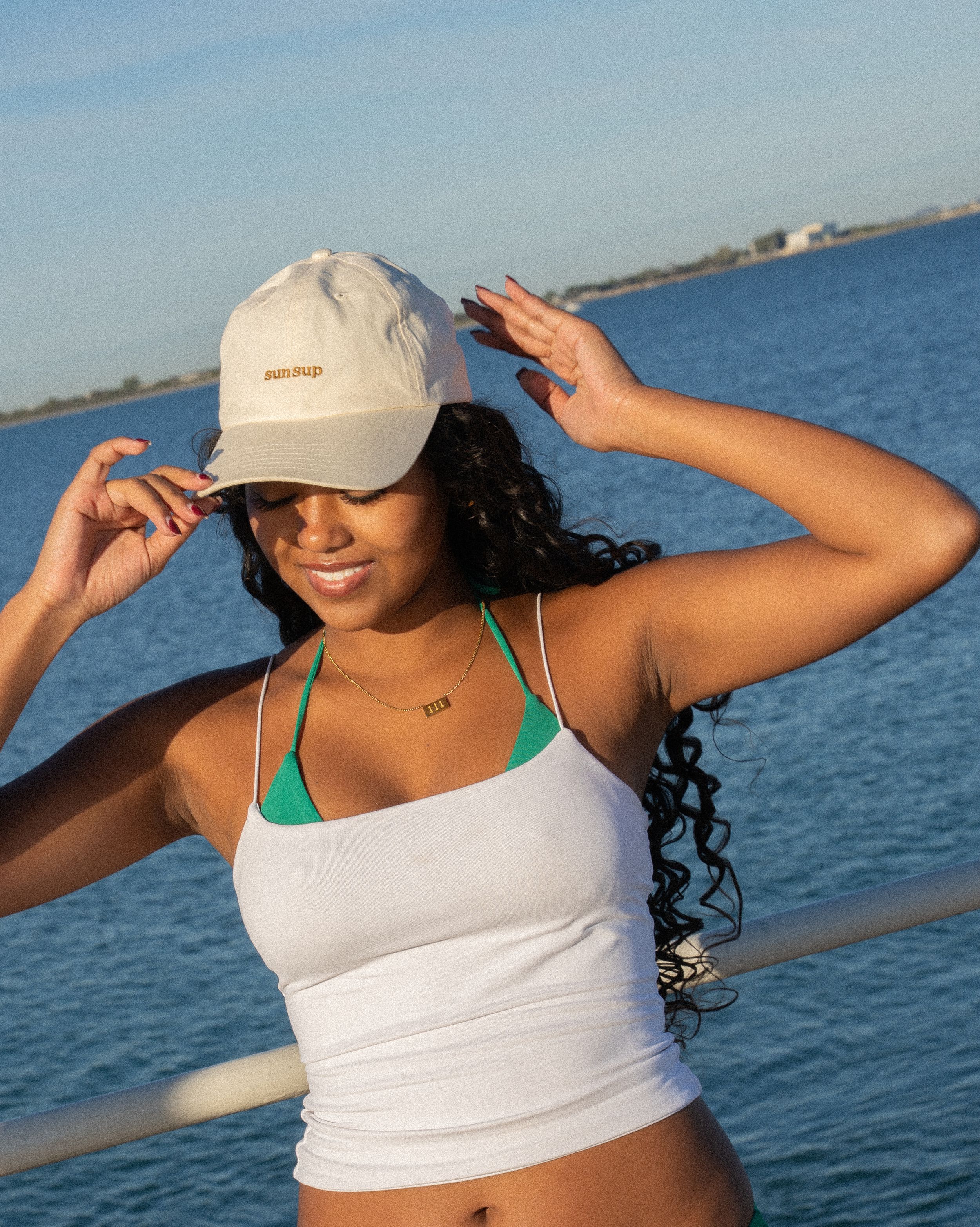 Person in white tank top and cap enjoying sunny day by the water.