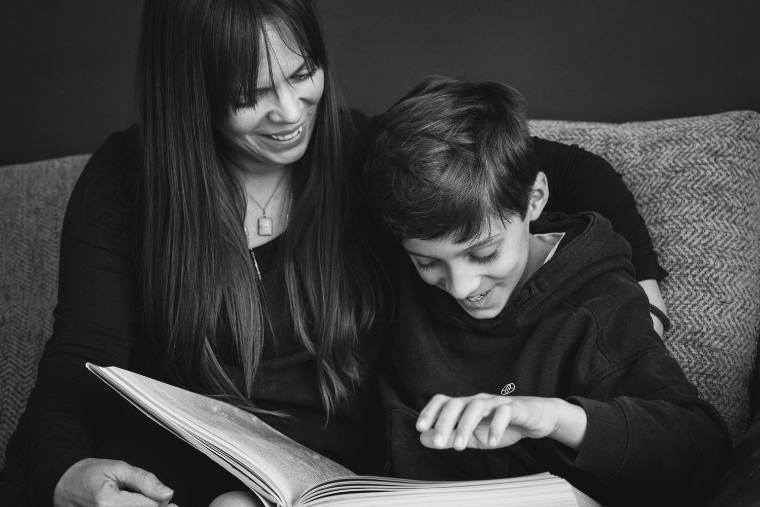 A touching black and white moment of parent and child sharing a book together on a couch.