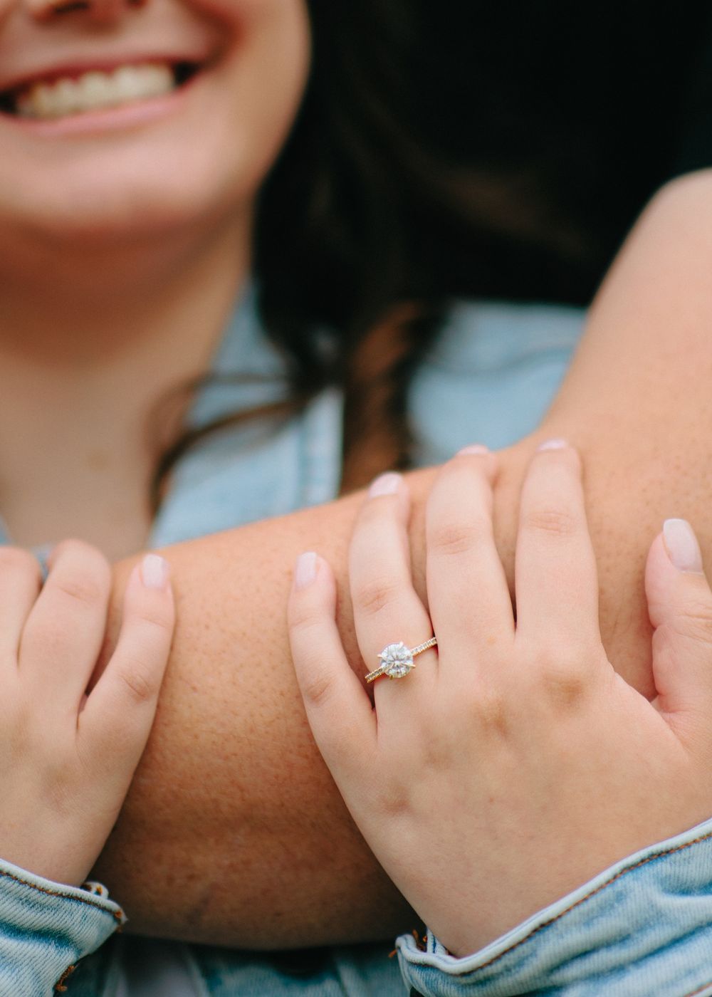Close-up view of hands wearing denim showing off a sparkling engagement ring.