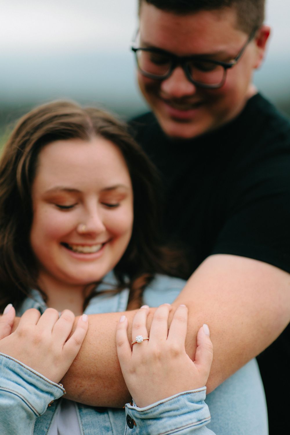 Close-up engagement photo showing couple embracing with diamond ring visible on womans finger.