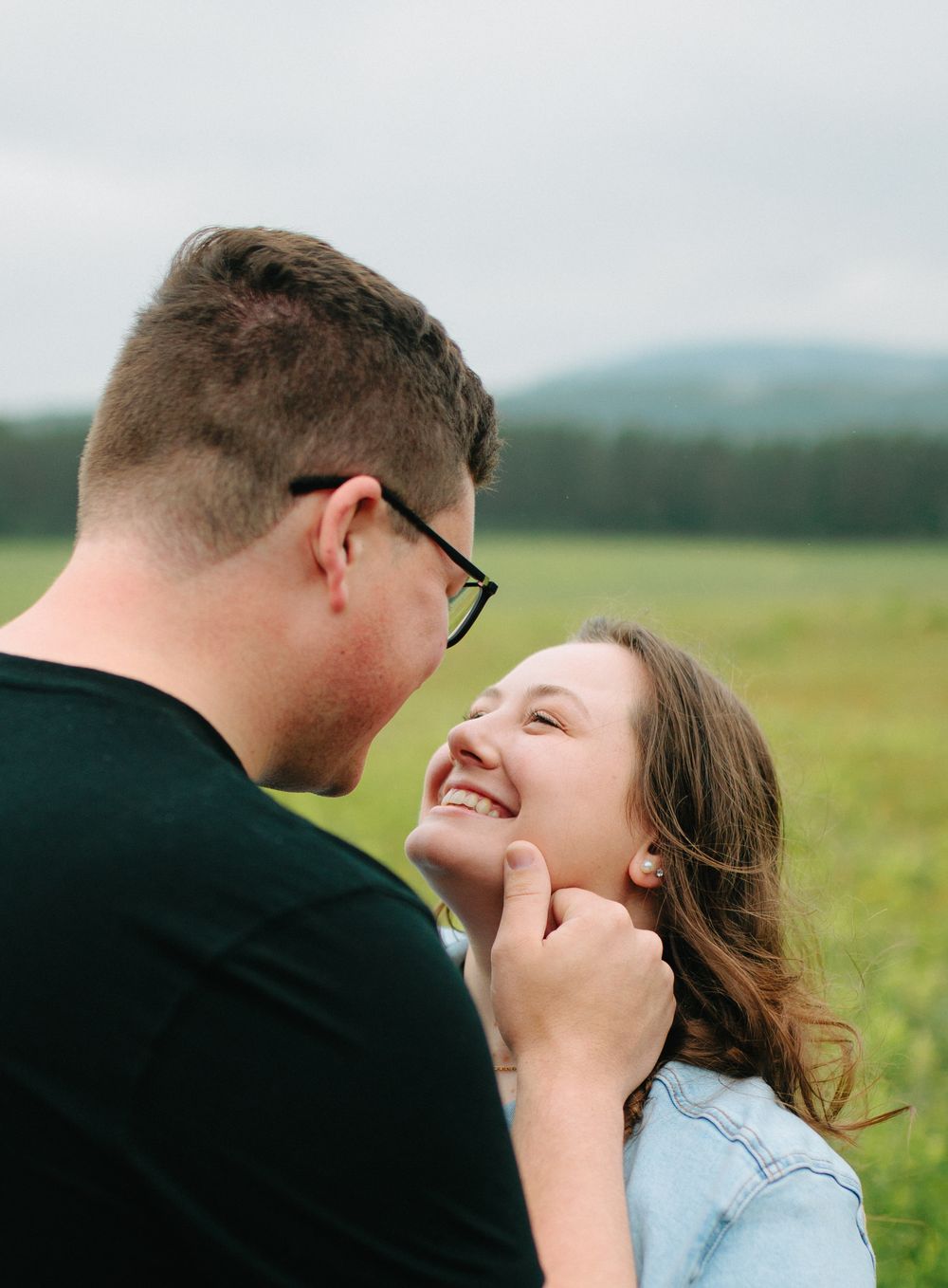 A couple shares a joyful moment together while laughing in a sunny field with natural lighting.
