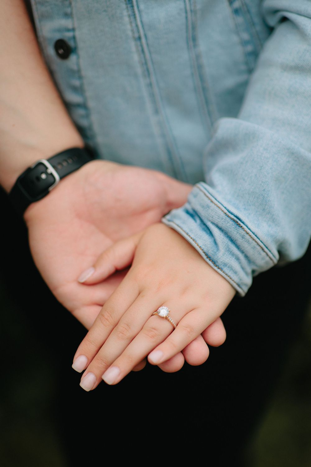 A close-up shot of hands clasped together showing an engagement ring, with denim clothing visible in the frame.