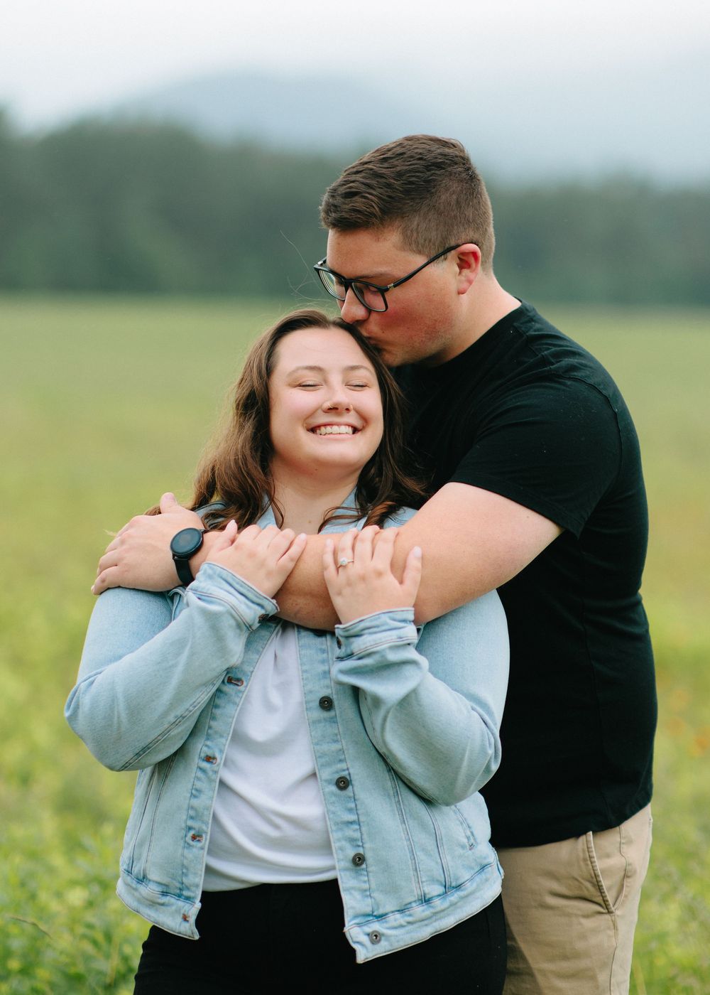 A joyful romantic moment shared between a couple embracing in a green field on an overcast day.