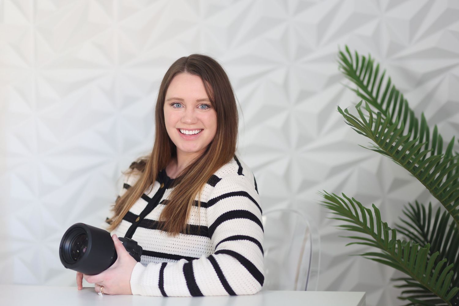 Professional photographer with camera against textured white wall with palm frond decor.
