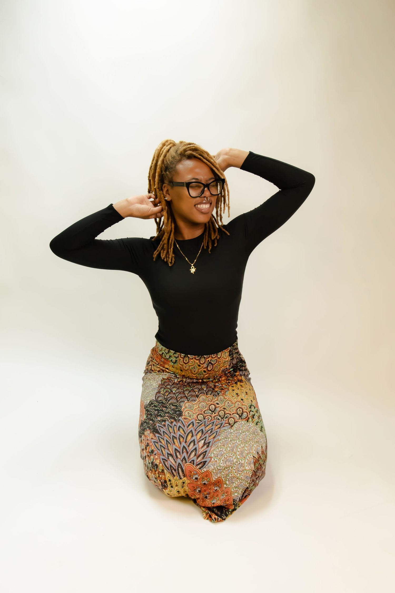 Figure in black long sleeve top and patterned skirt poses dynamically against white background.