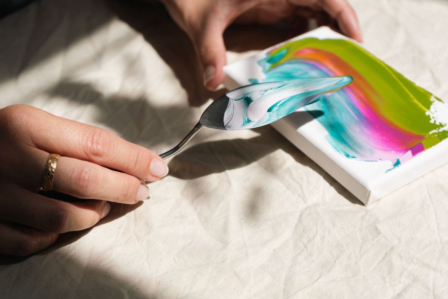 Artist's hands holding a pallet knife and canvas under dappled sunlight, retainer brand photography for Surrey artist.