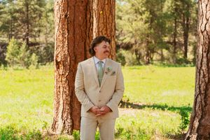 A happy pair laughs and embraces among tall evergreen trees in a sunny meadow during an outdoor photoshoot.