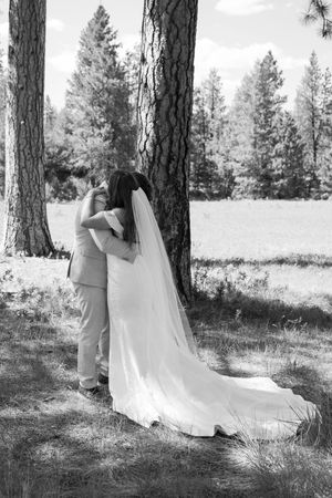 A romantic black and white wedding photo shows a couple sharing an intimate moment beneath tall pine trees.