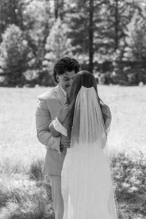 A black and white wedding photo captures two people sharing an intimate moment in a sunny outdoor field.