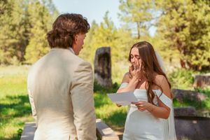 A couple shares an emotional moment during their outdoor wedding ceremony in a sunny forest setting.