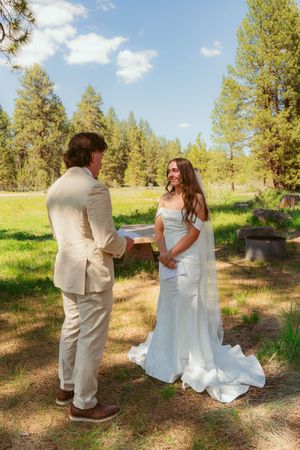 Newlyweds share playful moments in a forest clearing on their wedding day.