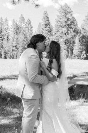 A romantic black and white photo series showing a couple in white attire sharing tender moments outdoors against a wooded backdrop.