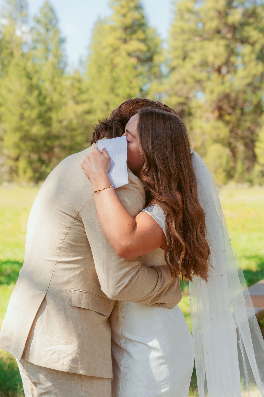 An intimate wedding embrace in a forest meadow with golden sunlight filtering through the pine trees.