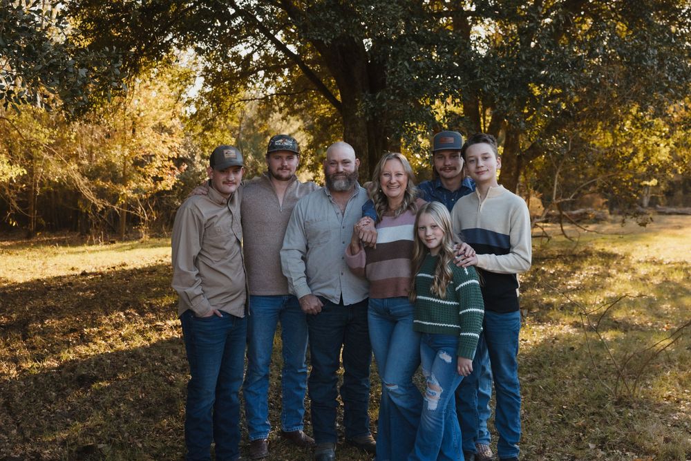 Family of seven wearing coordinated denim and neutral colors pose together outdoors during golden hour sunset in nature.