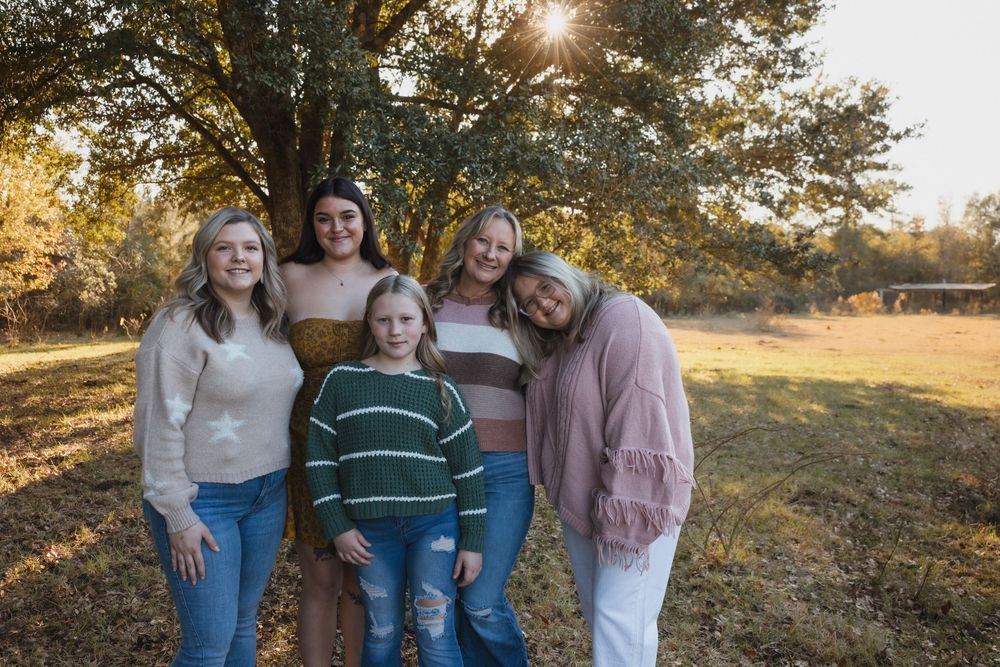 A group poses together for an outdoor portrait under a large tree with sunlight peeking through the branches.