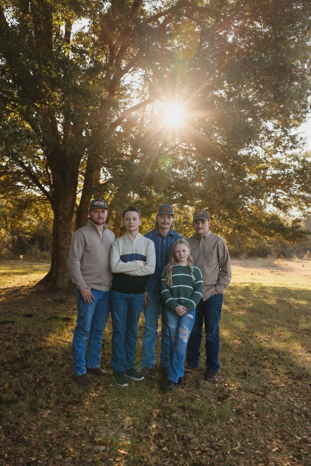 A group poses for a photo in autumn sunlight with trees and fallen leaves in the background.