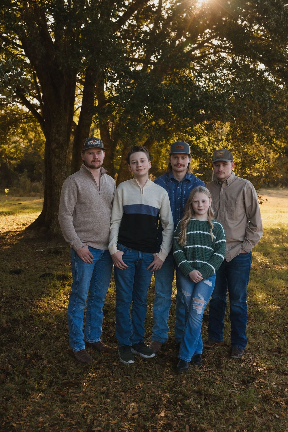 A small group poses together on fallen autumn leaves at sunset in a wooded setting.