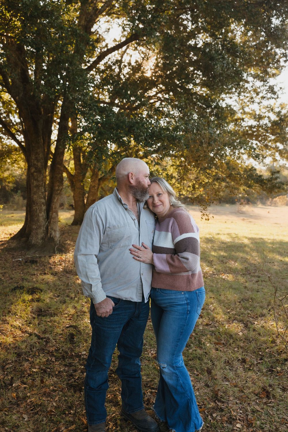 Couple embracing in a wooded area during golden hour with sunlight streaming through fall foliage.