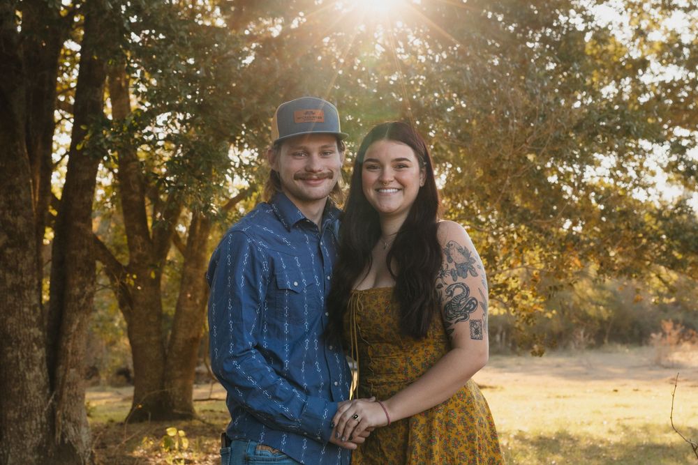 A couple embraces in a golden sunlit forest setting during an outdoor photo session at sunset.