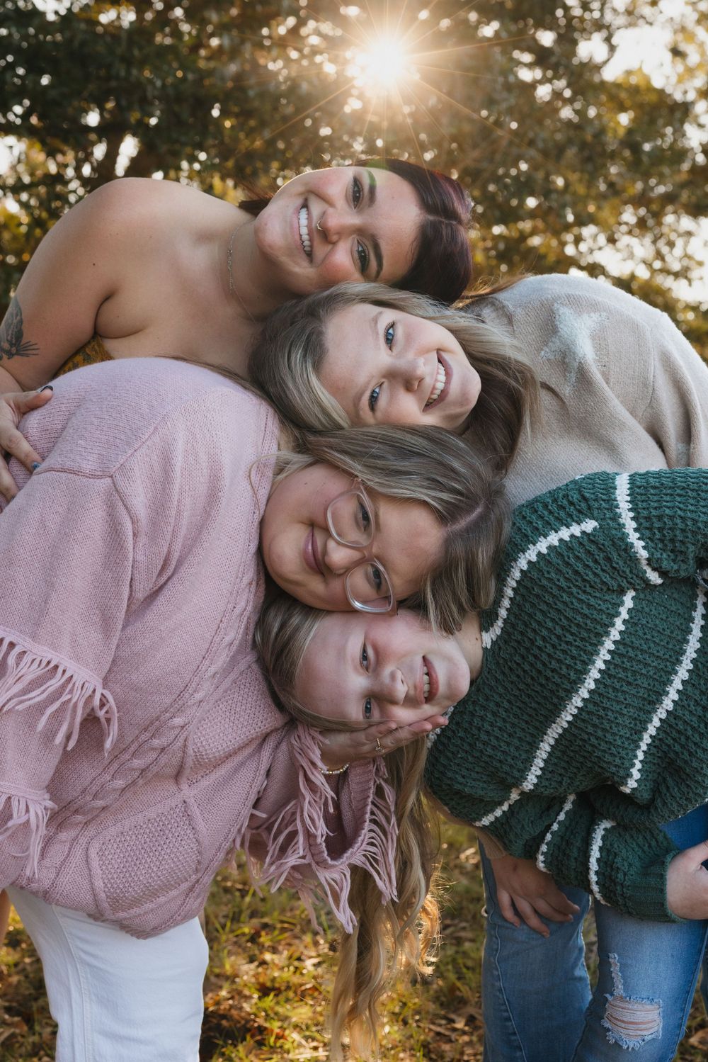Friends pose together laughing and leaning on each other outdoors during golden hour sunlight in autumn.