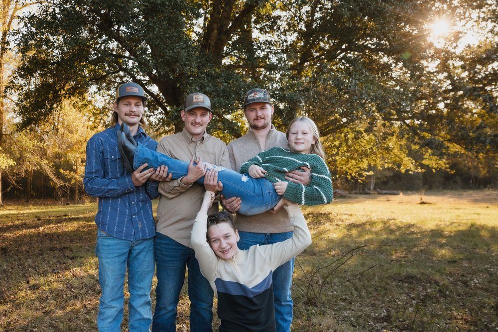 Group in casual clothing standing together in an autumn landscape with golden sunlight filtering through trees.