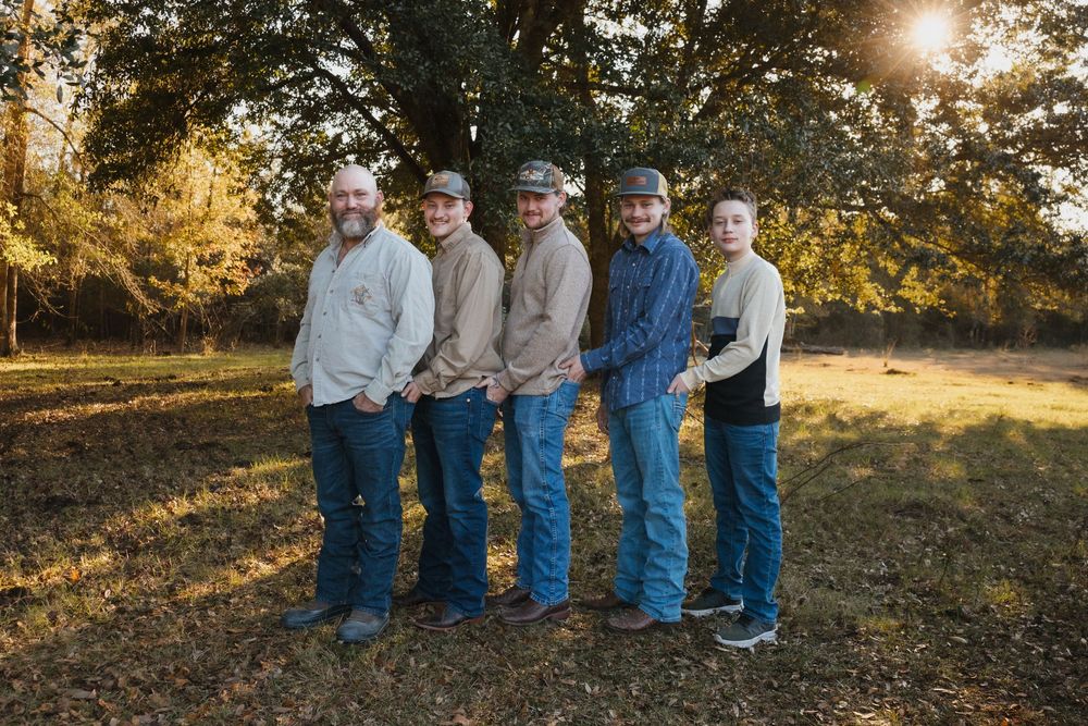 A group of five people wearing casual clothing stand together outdoors at sunset in an autumn setting.