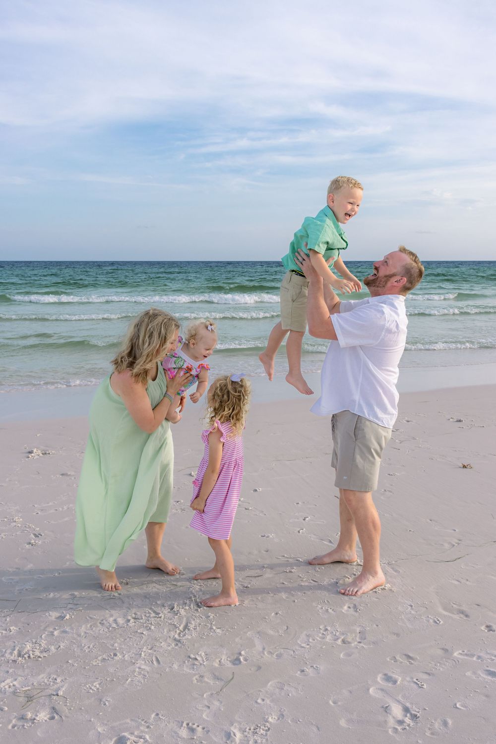 Family playing together on a white sandy beach at sunset with ocean waves in the background.