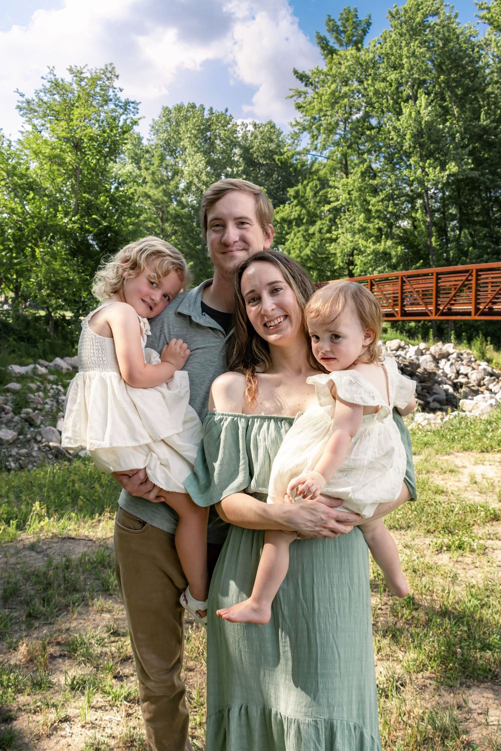 A joyful outdoor family photoshoot in a grassy area with people wearing sage green and cream colored outfits.