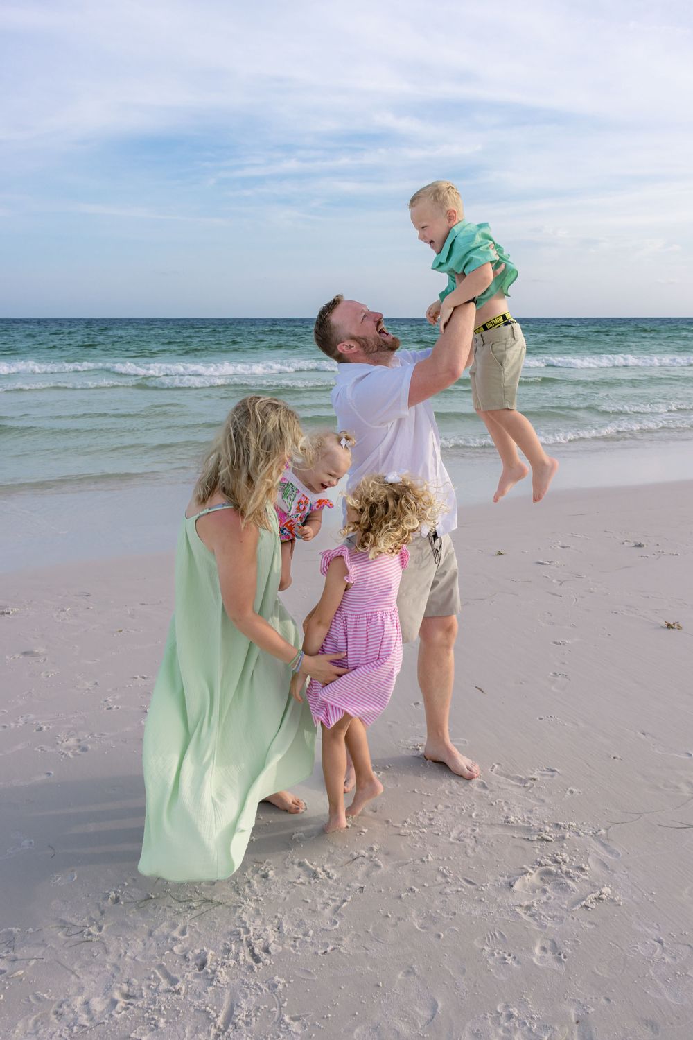 Playful beach moments captured as family members lift and swing each other by the ocean.