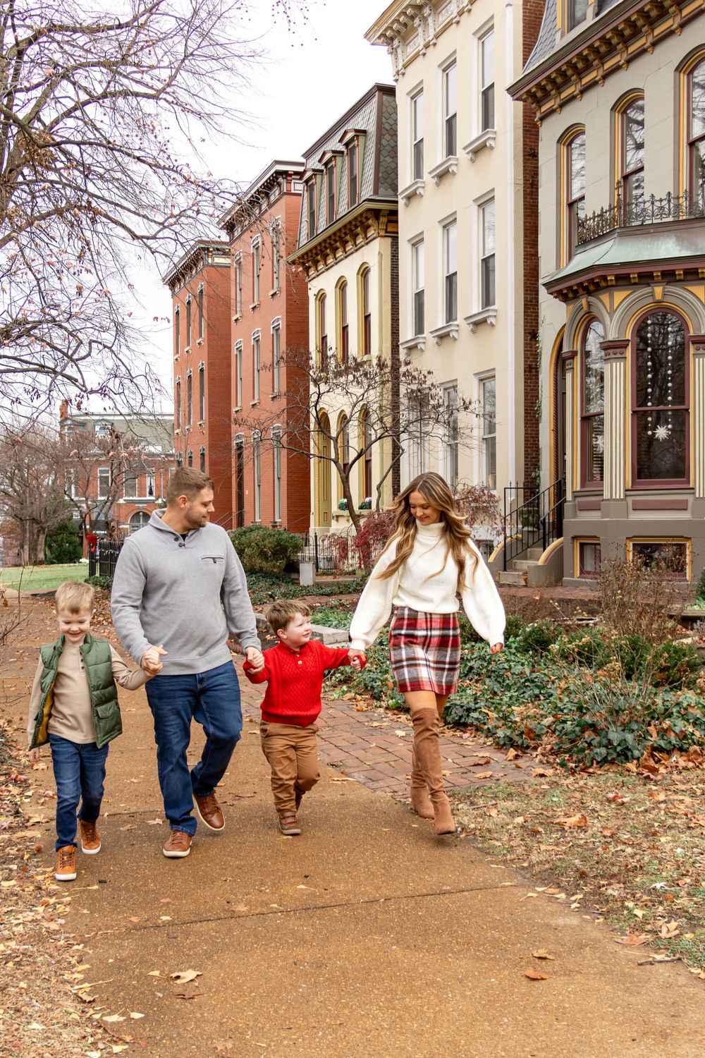 Family walking together on a path beside historic brownstone buildings during autumn.
