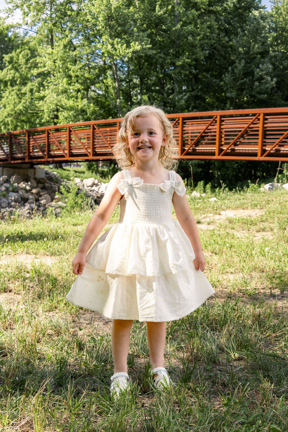 A small child in a white dress twirls and plays in a grassy outdoor setting.