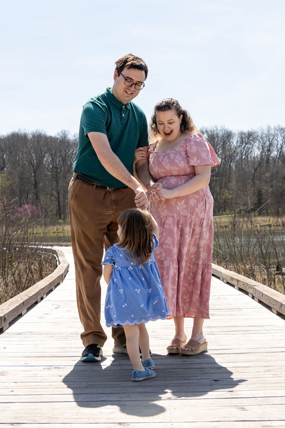 Family members dancing and twirling together on a wooden boardwalk surrounded by nature.
