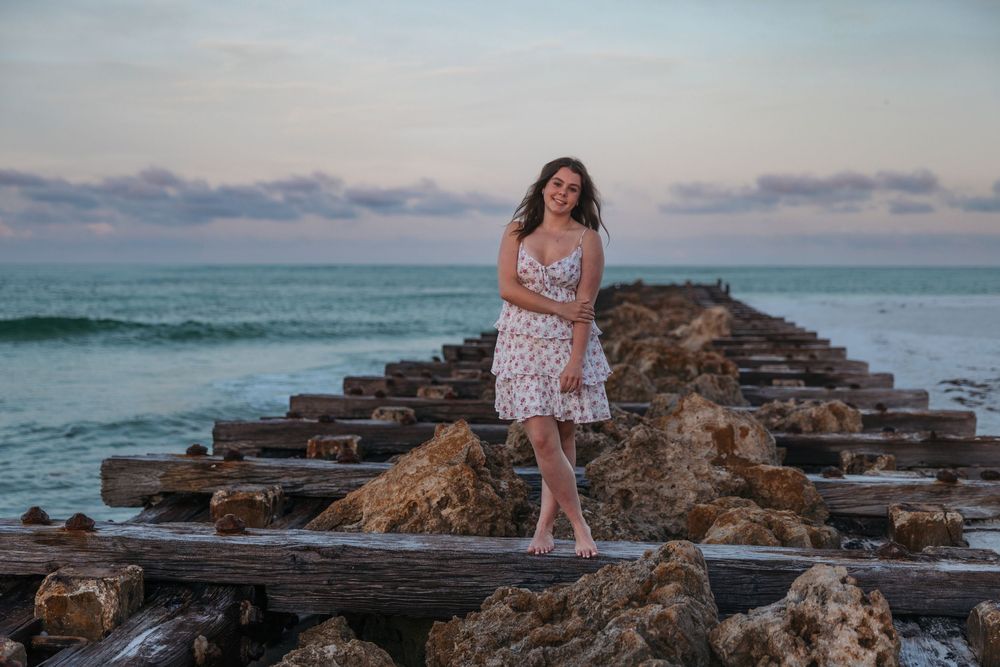 A floral dress silhouette against the ocean backdrop on a rocky pier during sunset.