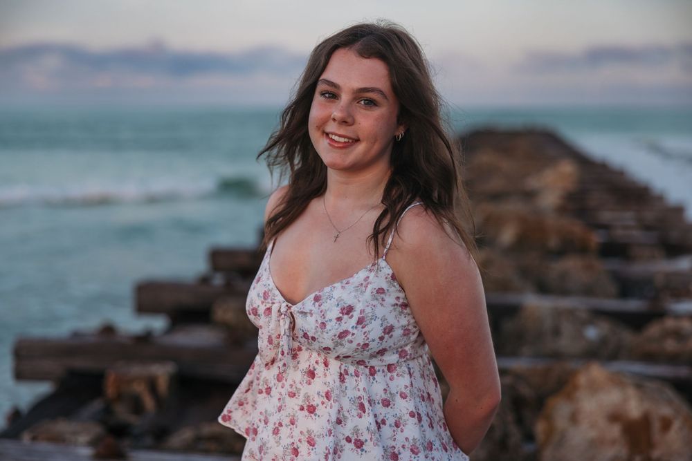 A floral sundress stands out against rocky coastal scenery and turquoise waters at sunset.